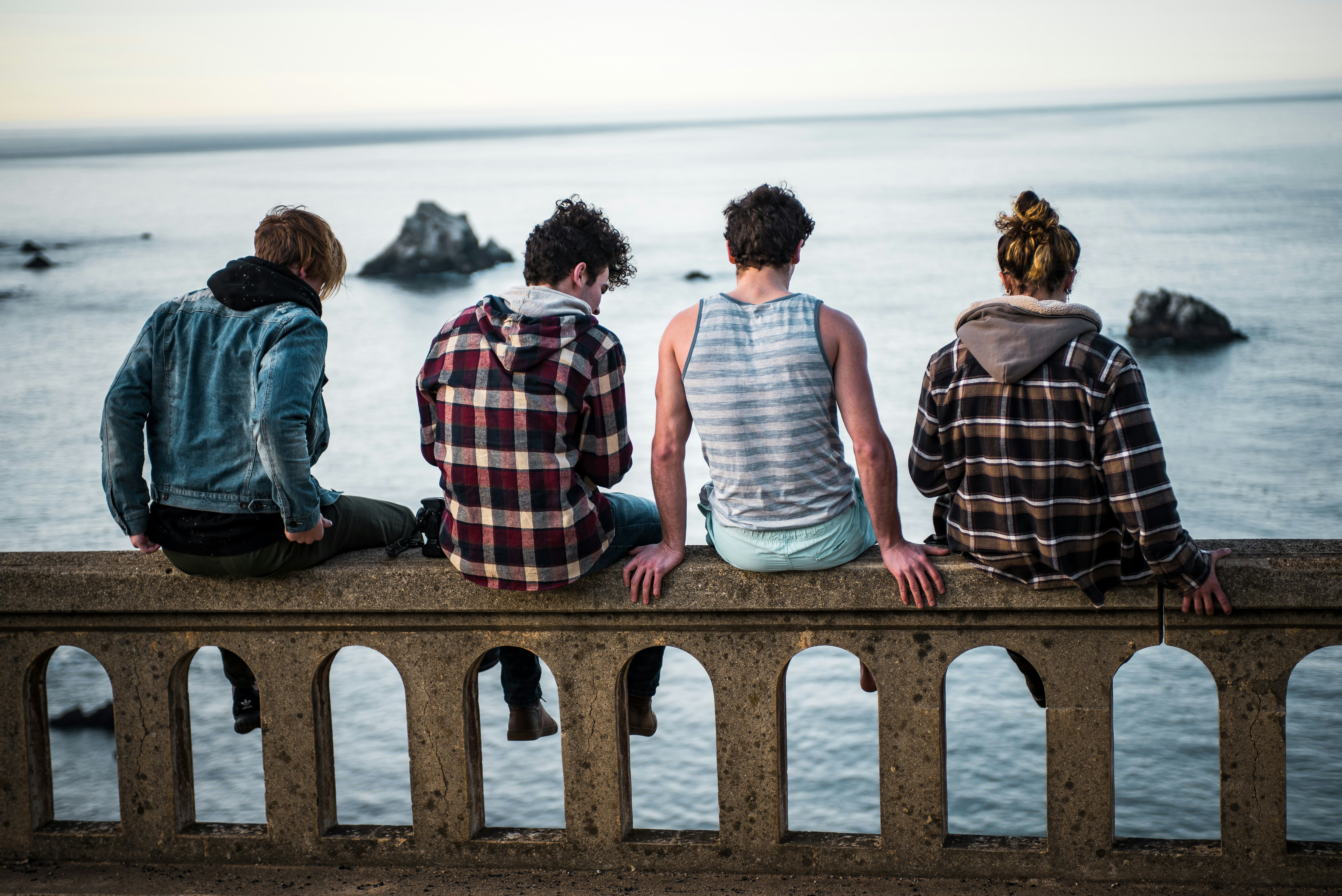 four person sitting on bench in front of body of water